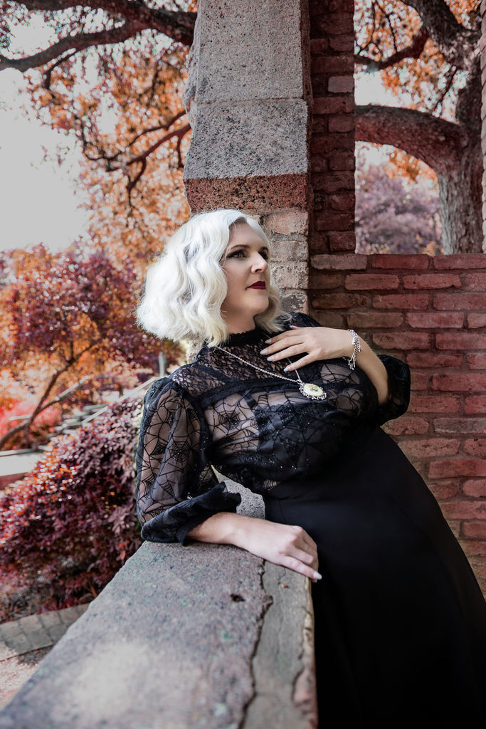 silver haired model wearing sheer black lace blouse with spider webs